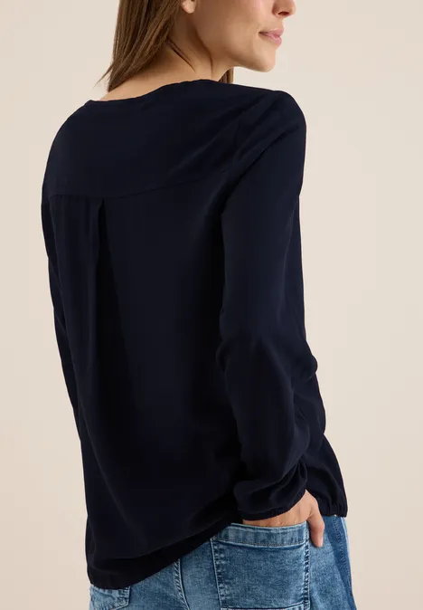Frau mit dunkelblauer Bluse und Jeans, von hinten zu sehen.